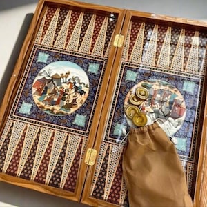 Könnte beinhalten: Ein Backgammon-Set aus Holz mit aufwendigen Designs. Das Spielbrett zeigt eine detaillierte Illustration in einem blau-weißen Rahmen. Das Set enthält goldfarbene Spielsteine und einen braunen Kordelzugbeutel zur Aufbewahrung.