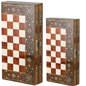May include: Two wooden chess and backgammon game sets. The sets feature a checkerboard pattern in brown and white, with ornate inlaid designs around the edges. The cases are rectangular with a dark finish and metal clasps. The larger set is approximately 18 inches tall.