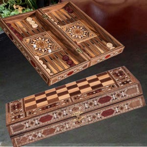 Puede incluir: Un juego de backgammon de madera con diseños de estrella incrustados y un tablero de ajedrez. El tablero de backgammon presenta triángulos de madera clara y oscura, dados y fichas. El tablero de ajedrez es un patrón de tablero de ajedrez con un borde decorativo.