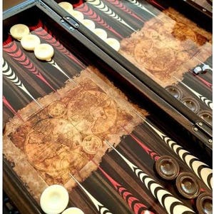 Könnte beinhalten: Ein Backgammon-Brett aus Holz mit dunklem Finish, das ein Vintage-Kartendesign auf der Spielfläche aufweist. Das Brett enthält weiße und braune Spielsteine sowie rot-weiße pfeilförmige Markierungen.