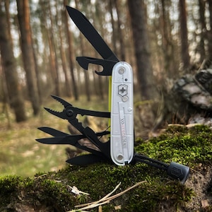 May include: A multi-tool with a clear and yellow handle, featuring various black tools including a knife, pliers, and bottle opener. The tool is open, displaying its components. The word "VICTORINOX" is printed on the handle. A black lanyard is attached.