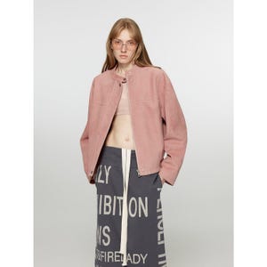May include: A dusty rose suede jacket with a round collar and a zipper closure. The model is wearing pink-tinted glasses and a gray skirt with white text. The skirt has the text "EXHIBITION" and "FIRE LADY".