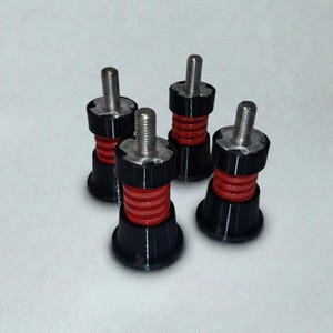 May include: Four black and red adjustable furniture feet with silver threaded posts. The feet have a black base, a red central section, and a black top section. The threaded posts are made of silver metal.