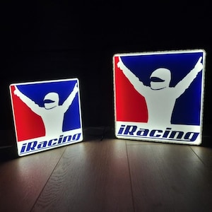 Könnte beinhalten: Zwei quadratische, beleuchtete Schilder mit dem iRacing-Logo. Jedes Schild zeigt eine weiße Silhouette eines Fahrers mit erhobenen Armen vor einem geteilten roten und blauen Hintergrund, mit dem blauen Schriftzug iRacing am unteren Rand.