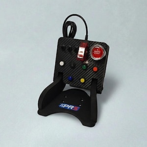 May include: A black control panel with a carbon fiber texture, featuring various colored buttons, switches, and a red start button. The panel is mounted on a black stand with the text "XPR5" in blue and white.