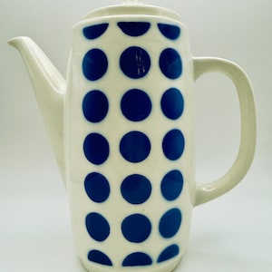 May include: A tall, off-white ceramic coffee pot with a lid and handle. The pot is decorated with a pattern of large, evenly spaced blue polka dots. The spout is long and curved.