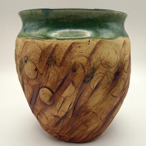 May include: A ceramic vase with a wide, flared rim featuring a glossy, deep green glaze. The body of the vase has a textured, unglazed tan surface decorated with impressed circular patterns and diagonal brown brushstrokes across the exterior.