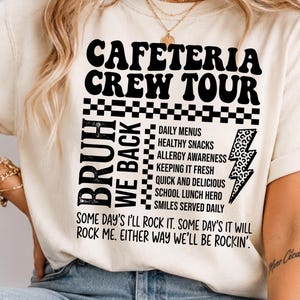 Può includere: Una t-shirt a maniche corte color crema con testo nero che recita CAFETERIA CREW TOUR, BRUH WE BACK, e un elenco che include DAILY MENUS, HEALTHY SNACKS, ALLERGY AWARENESS, KEEPING IT FRESH, QUICK AND DELICIOUS, SCHOOL LUNCH HERO, SMILES SERVED DAILY.