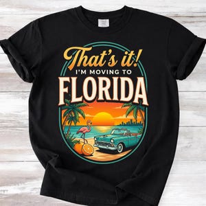 May include: A white ceramic mug with a black handle and the text "But First, Coffee" in a bold, black font. The mug is set against a blurred background. The mug appears to be approximately 10 cm tall.