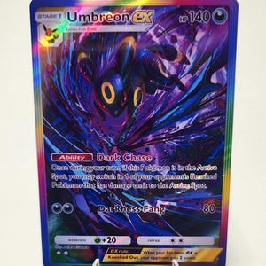 May include: A holographic Umbreon ex Pokémon card. The card features a dark blue and purple background with the Umbreon character in the center. Text includes "Dark Chase" and "Darkness Fang".