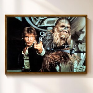 Könnte beinhalten: Ein gerahmtes Star Wars-Filmplakat mit Han Solo, der eine Blasterpistole hält, und Chewbacca. Das Poster hat einen braunen Holzrahmen und hängt an einer weißen Wand. Ein klassisches Filmbild.