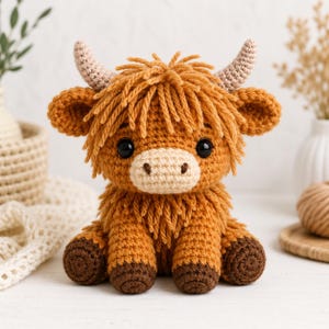 May include: A crocheted Highland cow soft toy. The plushie has a light brown muzzle, dark brown hooves, and light brown horns. The cow has a shaggy, light brown mane and body. The eyes are black.