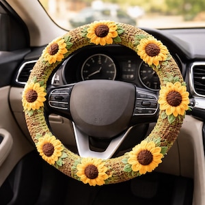 May include: A crochet steering wheel cover featuring a sunflower design. The cover is brown and green with yellow sunflowers and green leaves. The steering wheel is black.