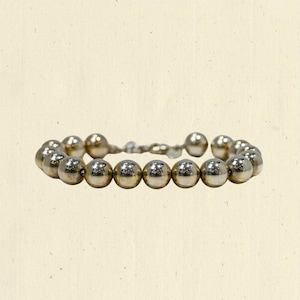 May include: A silver beaded bracelet. The bracelet is made of small, round, metallic beads strung together. The beads have a shiny, reflective surface. The bracelet is displayed on a neutral background.