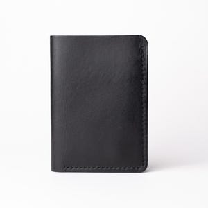 Puede incluir: Una cartera de cuero negro, rectangular y vista verticalmente. La cartera está cerrada, con una superficie lisa y mate. Los bordes son redondeados y las costuras son visibles en los laterales. El fondo es blanco liso.