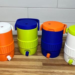 May include: Four colorful water coolers in orange, green, blue, and white, each with a matching lid and spigot. The coolers are cylindrical with a ribbed design around the base and a handle on top. They are arranged on a wooden surface.