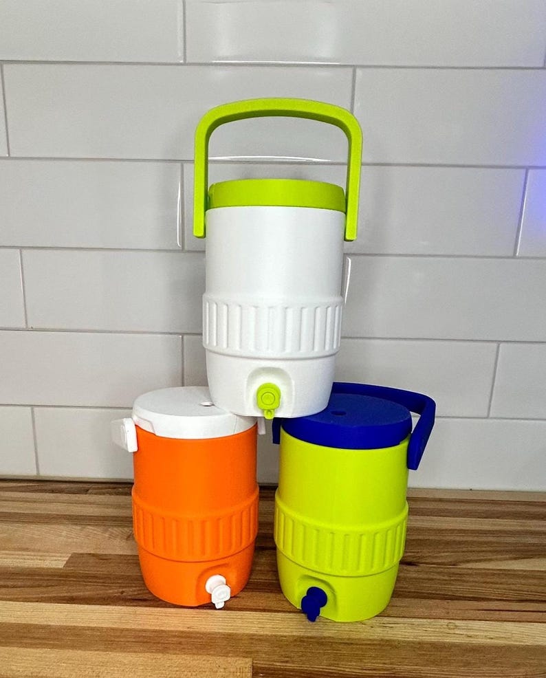 May include: Three colorful water coolers. The top cooler is white with a green handle and lid. The middle cooler is orange with a white lid. The bottom cooler is yellow with a blue handle and lid. Each cooler has a spigot.