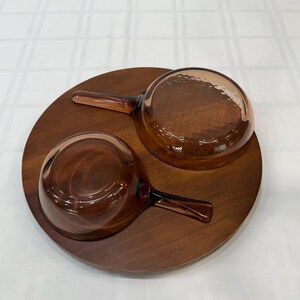 Puede incluir: Dos cuencos de vidrio marr&oacute;n con asas sobre una bandeja redonda de madera. Los cuencos tienen un interior texturizado y son de color &aacute;mbar. La bandeja de madera es de color marr&oacute;n oscuro y tiene un acabado liso. El juego es ideal para servir sopas o salsas.