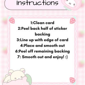May include: A pink and white illustrated card with instructions for a sticker. The text reads "Instructions" at the top, followed by numbered steps. Strawberry and bear illustrations decorate the card.