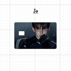 May include: A rectangular card with a portrait of a person wearing glasses and a black outfit. The card has a white rectangle in the upper left corner. The word "Jo" is above the card.