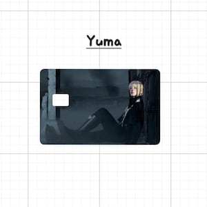 May include: A rectangular card with a photograph of a person in black clothing, with the name "Yuma" above the card. The person is seated, with blonde hair and a dark background. The card has a white rectangle in the upper left corner.