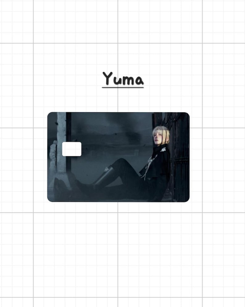 May include: A rectangular card with a photograph of a person in black clothing, with the name "Yuma" above the card. The person is seated, with blonde hair and a dark background. The card has a white rectangle in the upper left corner.