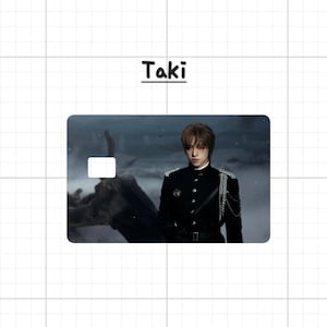 May include: A rectangular card with the name "Taki" above it. The card features an image of a person in a black uniform with silver chain accents. The background is a blurred, dark landscape.