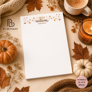 May include: A white notepad featuring the text Hello autumn and LISA'S NOTES at the top, decorated with orange and brown leaf illustrations. The notepad is surrounded by pumpkins, dried foliage, a coffee mug, and a candle, with text stating Available in A4, A5 & Slimline.