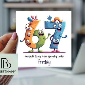 May include: A birthday card with the numbers 67 depicted as cartoon characters with multiple eyes and limbs. The card has the text "Happy birthday to our special grandson Freddy". The card is held in a person's hand.