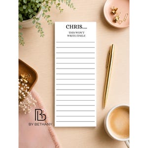 May include: A rectangular white notepad with black horizontal lines and the text CHRIS.... THIS WON'T WRITE ITSELF. at the top. The notepad is positioned vertically on a light-coloured surface next to a gold pen, a coffee cup, and office supplies.