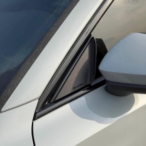 May include: Close-up of a white car's side mirror and window frame. The mirror is white, and the window frame is black. The car's body is white, and the text "Good Line" is visible on the black trim.