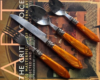 Juego de cubiertos de acero inoxidable con mangos de acrílico perlado color ámbar y detalles decorativos en tono plateado, 16 piezas.