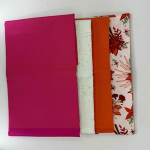 May include: A collection of folded fabric pieces in various colors and patterns. The fabrics include a solid magenta, a white fabric with gold speckles, a solid orange, and a floral print with red and green accents on a light pink background.