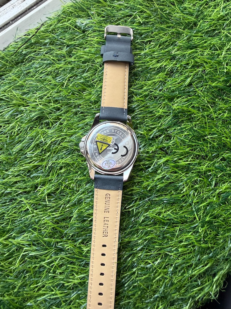 May include: A wristwatch with a black leather band and a silver-colored stainless steel case. The watch band is attached with a silver buckle. The back of the watch case has the text "Stainless Steel" and other markings.