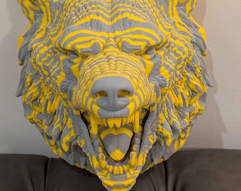 May include: A striking, three-dimensional wolf head sculpture. The sculpture features a detailed design with alternating yellow and gray stripes, creating a textured appearance. The wolf's mouth is open, revealing its teeth and tongue. The sculpture is mounted on a wall.