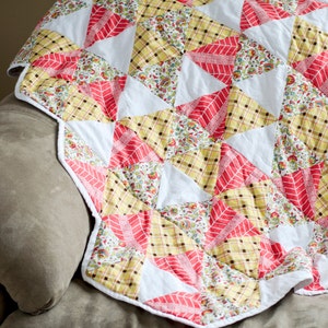 May include: A patchwork quilt with a white background and red, yellow, and floral patterned triangles. The quilt is folded and draped over a brown couch.
