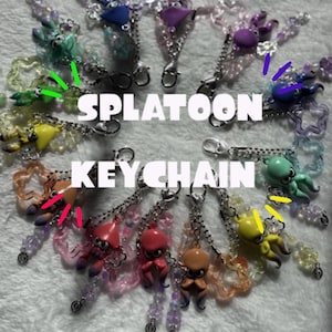 May include: A collection of colorful Splatoon keychains. Each keychain features a small octopus figure in various colors, including red, yellow, blue, and green, with beaded accents and a silver chain. The word "Splatoon" and "Keychain" are displayed in white text.