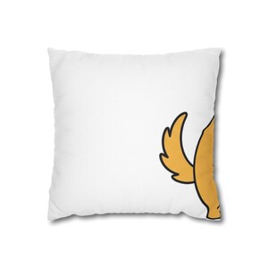 May include: White square pillow featuring a cartoon illustration of a golden-yellow dog tail with black outlines. The pillow is a decorative item, likely for a bed or couch.