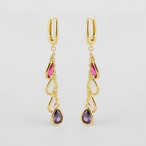 May include: A pair of gold-toned drop earrings featuring a hinged hoop closure. Each earring has a delicate chain suspending four teardrop-shaped charms in a gradient of colors, transitioning from a deep pink at the top to a dark purple at the base.