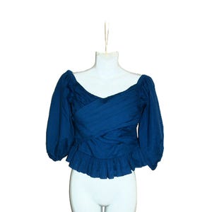 May include: A dark teal blouse with a wrap-style bodice and three-quarter sleeves. The blouse features a ruffled hem and is displayed on a white mannequin. The fabric appears to be a lightweight material.