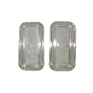 May include: Two rectangular, clear glass dishes with a silver-coloured, rounded border. The dishes have a slightly textured interior and are set against a white background. The dishes are likely for serving or display.