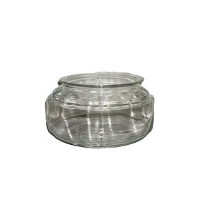 May include: A clear, round glass jar with a lid. The jar has a wide, low profile and a textured, geometric design. The lid fits snugly on top. The jar is empty and sits against a white background.