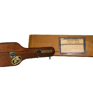 May include: A wooden Tru-Test tool with a metal hinge and a yellow label, positioned next to a rectangular cardboard box featuring a blue and white label that reads Wilson Bros. P.O. Box 811, Chicago, Ill. Springfield, Missouri.