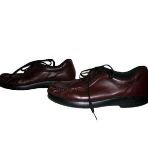 May include: A pair of burgundy leather shoes with black laces and soles. The shoes have a classic, casual design, suitable for everyday wear. The leather appears to be smooth and the soles are sturdy.