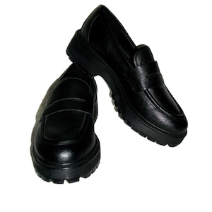 May include: A pair of black leather loafers with a chunky sole. The shoes have a classic penny loafer design with a rounded toe and a strap across the vamp. The soles are thick and textured.