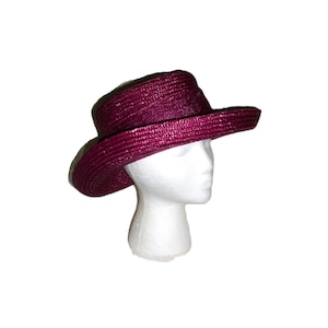 May include: A burgundy-colored hat with a wide brim and a structured crown. The hat is made of woven material and is displayed on a white mannequin head. The hat's design suggests it is suitable for sun protection or fashion.