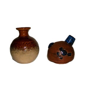 May include: Two ceramic pieces: a small, round vase with a brown and tan color scheme and a lid with a blue spout and dark blue floral accents. The vase has a narrow neck and a textured surface.