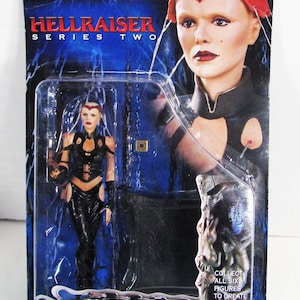 May include: A Hellraiser Series Two action figure of Angelique, packaged in a blue and black blister pack. The figure is wearing a black outfit with red accents. The packaging includes the text "COLLECT ALL SIX FIGURES TO CREATE YOUR OWN PILLAR OF SOULS."
