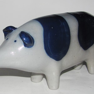 May include: A ceramic pig figurine with a white base and dark blue spots. The pig has a long snout, small ears, and four short legs. The figurine is a decorative item.
