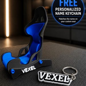 Op de afbeelding: Een miniatuur kuipstoel in racestijl in zwart en blauw met de tekst VEXEL op de zijkant, vergezeld van een bijpassende zwart-witte sleutelhanger met de tekst VEXEL en een zilveren metalen ring voor sleutels.